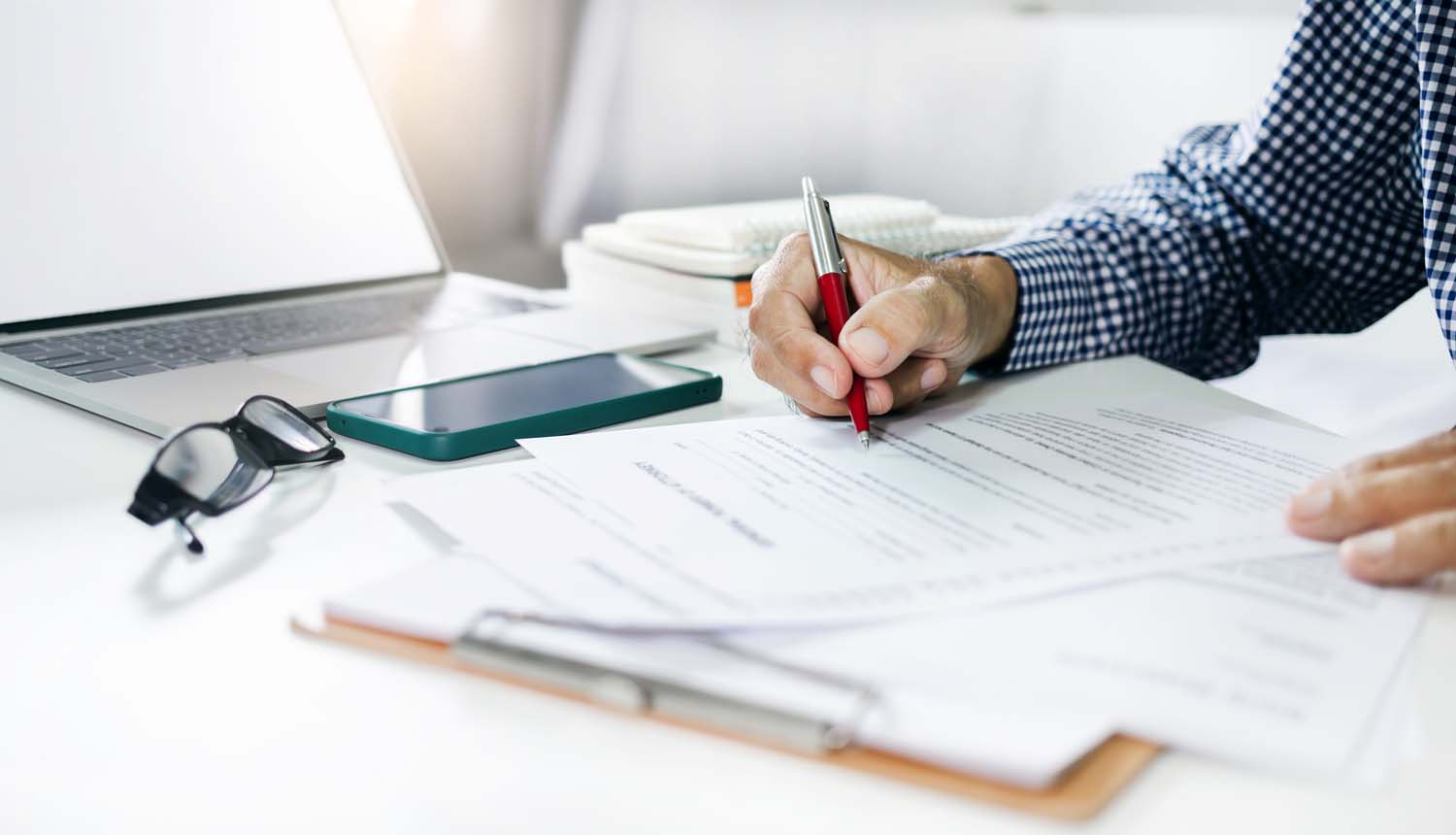 Person completing property tax paperwork at a desk with phone, glasses, and laptop